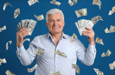 Senior man with American dollars under money rain on blue background
