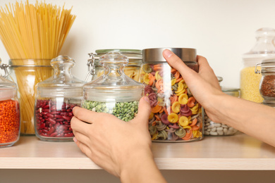 Woman taking jars of different products from wooden shelf, closeup