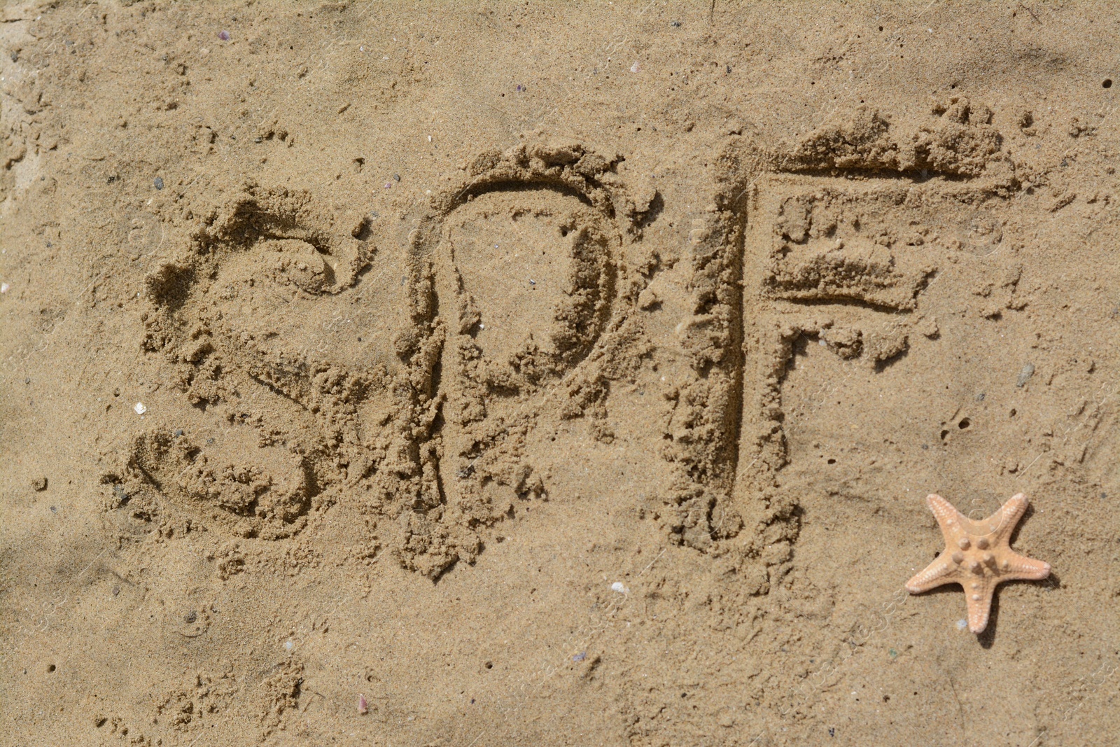 Photo of Abbreviation SPF written on sand and starfish at beach, top view