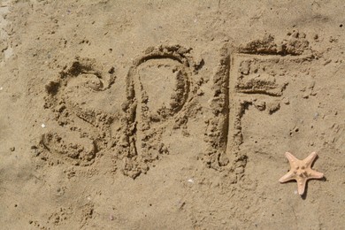 Abbreviation SPF written on sand and starfish at beach, top view
