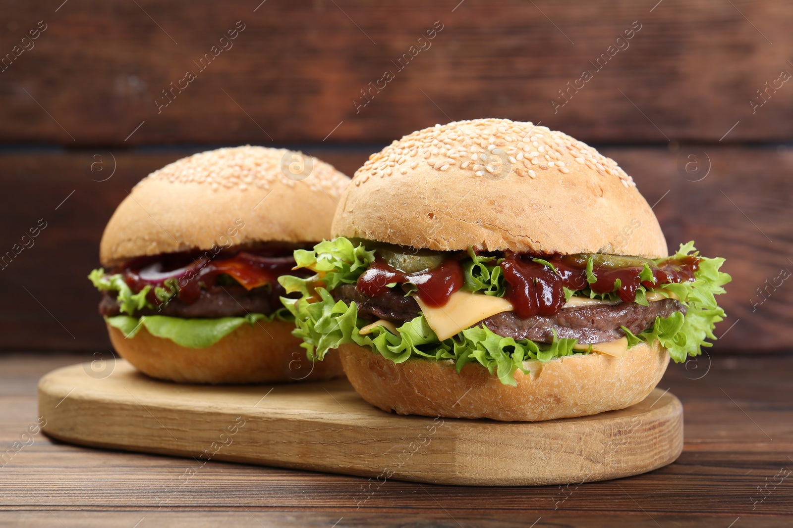 Photo of Board with delicious cheeseburgers on wooden table, closeup