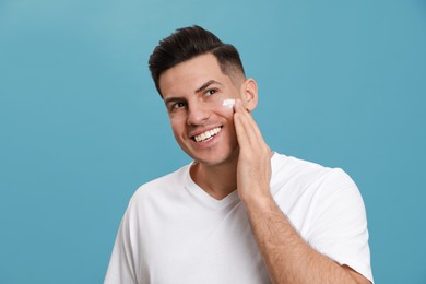 Photo of Happy handsome man applying face cream against turquoise background