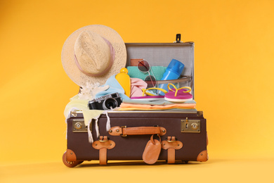 Open vintage suitcase with different beach objects packed for summer vacation on orange background