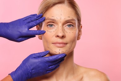 Photo of Doctor checking patient's face before cosmetic surgery operation on pink background, closeup
