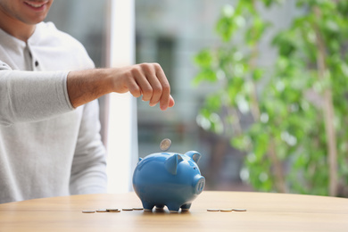 Man putting money into piggy bank at table, closeup. Space for text