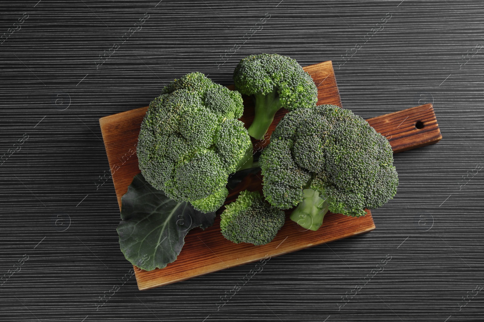 Photo of Board with fresh raw broccoli on black wooden table, top view