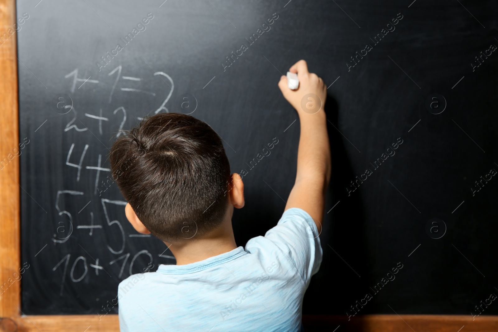 Photo of Little child with chalk doing math at blackboard