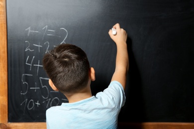 Photo of Little child with chalk doing math at blackboard