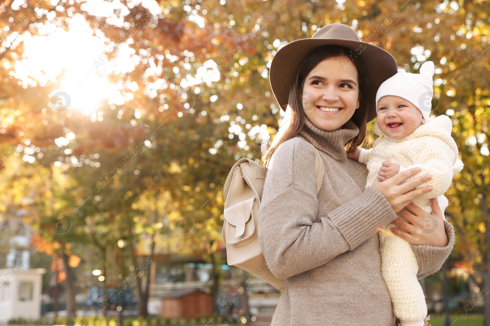 Photo of Happy mother with her baby daughter outdoors on autumn day, space for text