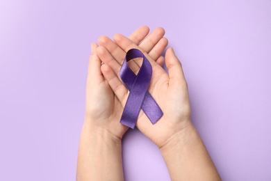 Woman holding purple ribbon on lilac background, top view. Domestic violence awareness