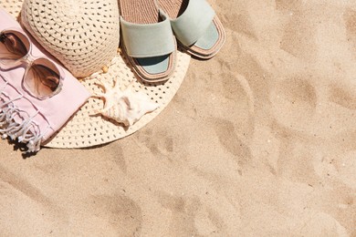 Straw hat, sunglasses, towel and slippers on sand, above view. Space for text