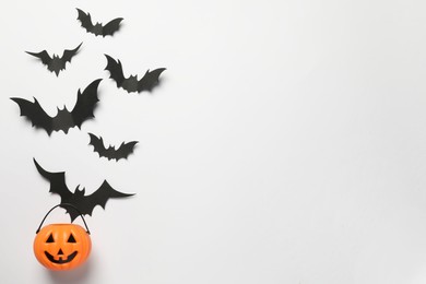 Photo of Flat lay composition with plastic pumpkin basket and paper bats on white background, space for text. Halloween celebration