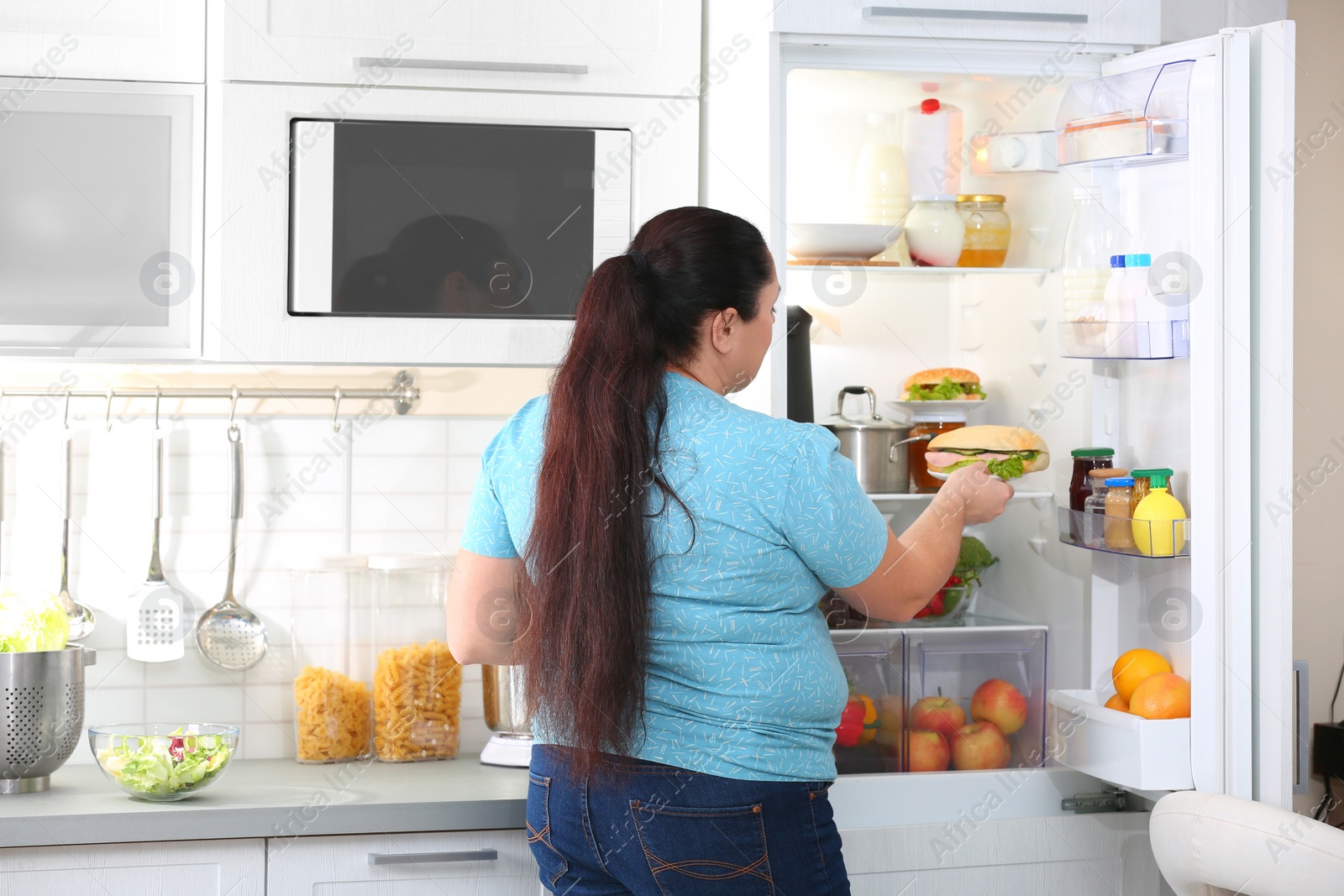Photo of Overweight woman taking sandwich from refrigerator in kitchen. Failed diet