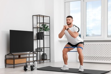 Athletic man doing exercise with elastic resistance band on mat at home