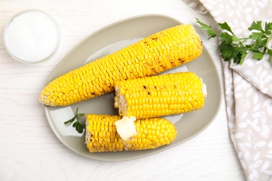 Photo of Fresh grilled corn cobs with butter on white wooden table, flat lay