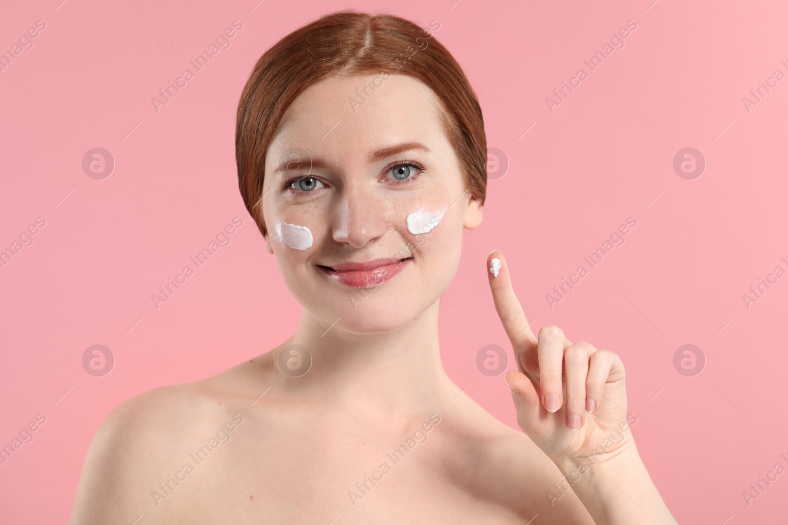 Photo of Beautiful woman with freckles and cream on her face against pink background