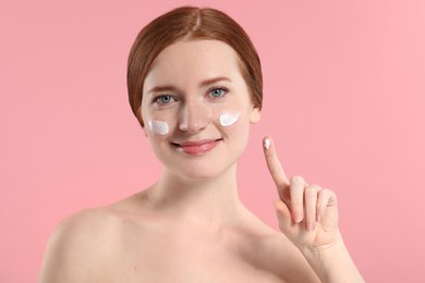 Photo of Beautiful woman with freckles and cream on her face against pink background