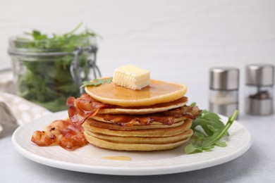 Delicious pancakes with bacon, butter and arugula on light table, closeup
