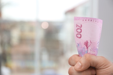 Photo of Man holding Ukrainian money in hand indoors, closeup. Space for text