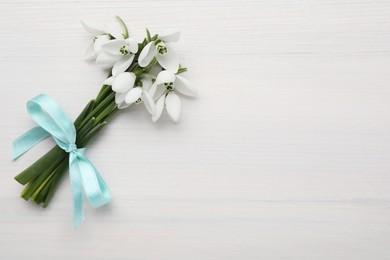 Beautiful snowdrop flowers with ribbon on white wooden table, top view. Space for text