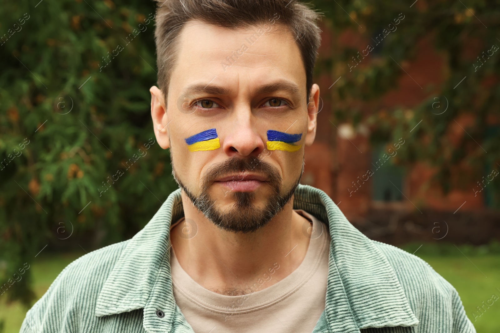 Photo of Man with drawings of Ukrainian flag on face outdoors