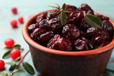 Photo of Tasty dried cranberries in bowl, fresh ones and leaves on table, closeup