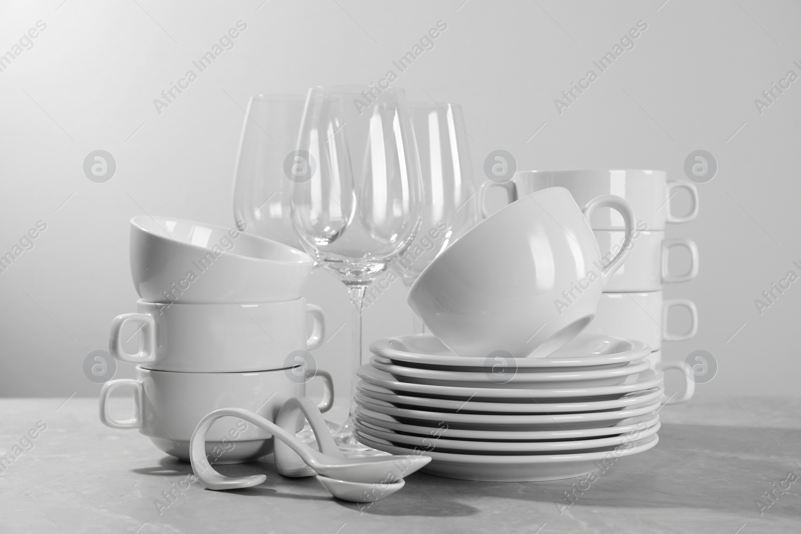 Photo of Set of clean dishware and glasses on grey table against light background
