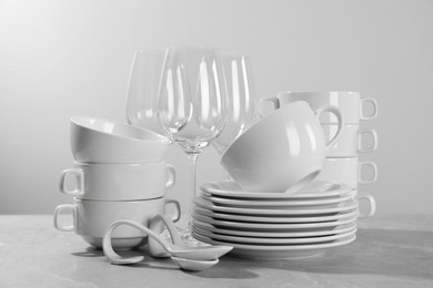 Set of clean dishware and glasses on grey table against light background