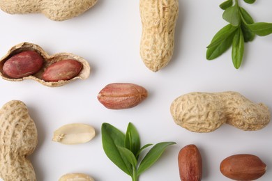 Fresh peanuts and leaves on white table, flat lay