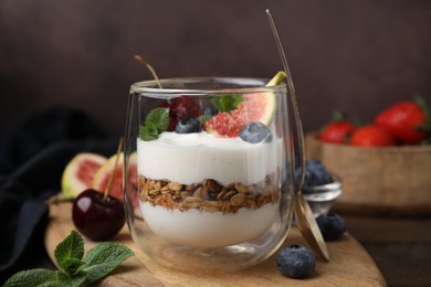 Glass with yogurt, berries, mint and granola on wooden table, closeup