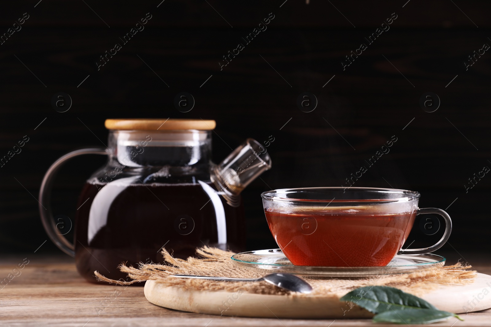 Photo of Aromatic hot tea in glass cup and teapot on wooden table. Space for text