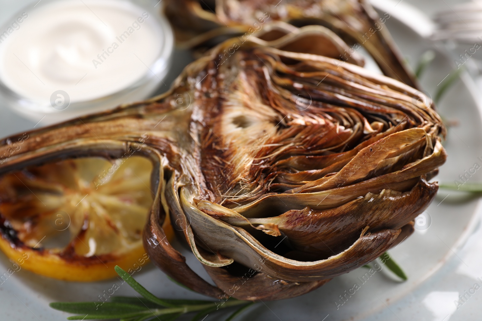 Photo of Tasty grilled artichoke, lemon slice and sauce on plate, closeup