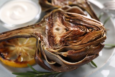 Photo of Tasty grilled artichoke, lemon slice and sauce on plate, closeup