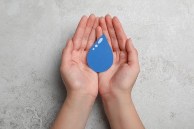 Photo of Save Water concept. Woman holding paper drop at light grey table, top view