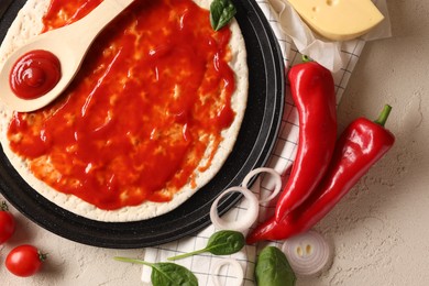 Pizza base smeared with tomato sauce and products on light textured table, flat lay