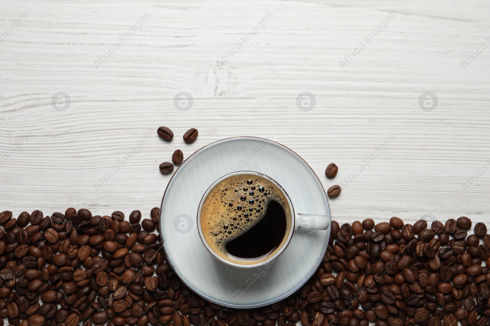 Photo of Cup of aromatic hot coffee and beans on white wooden table, flat lay. Space for text