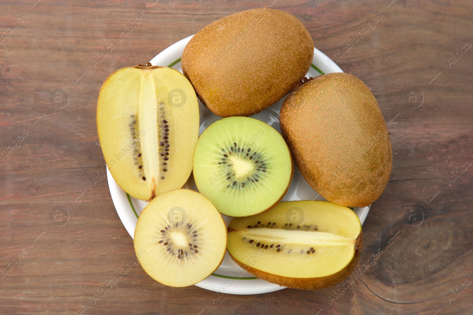 Photo of Plate with whole and cut fresh kiwis on wooden table, top view