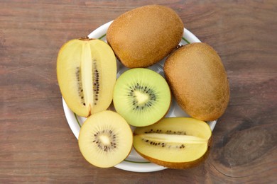 Photo of Plate with whole and cut fresh kiwis on wooden table, top view