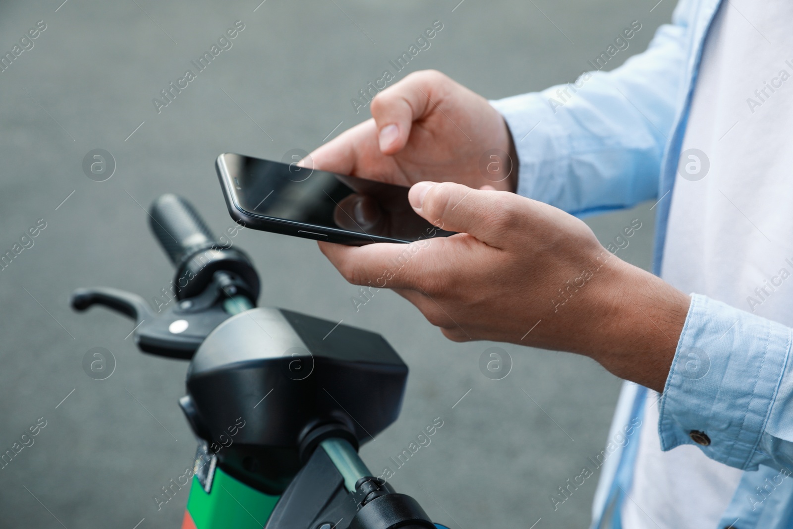 Photo of Man using smartphone to pay and unblock electric kick scooter outdoors, closeup