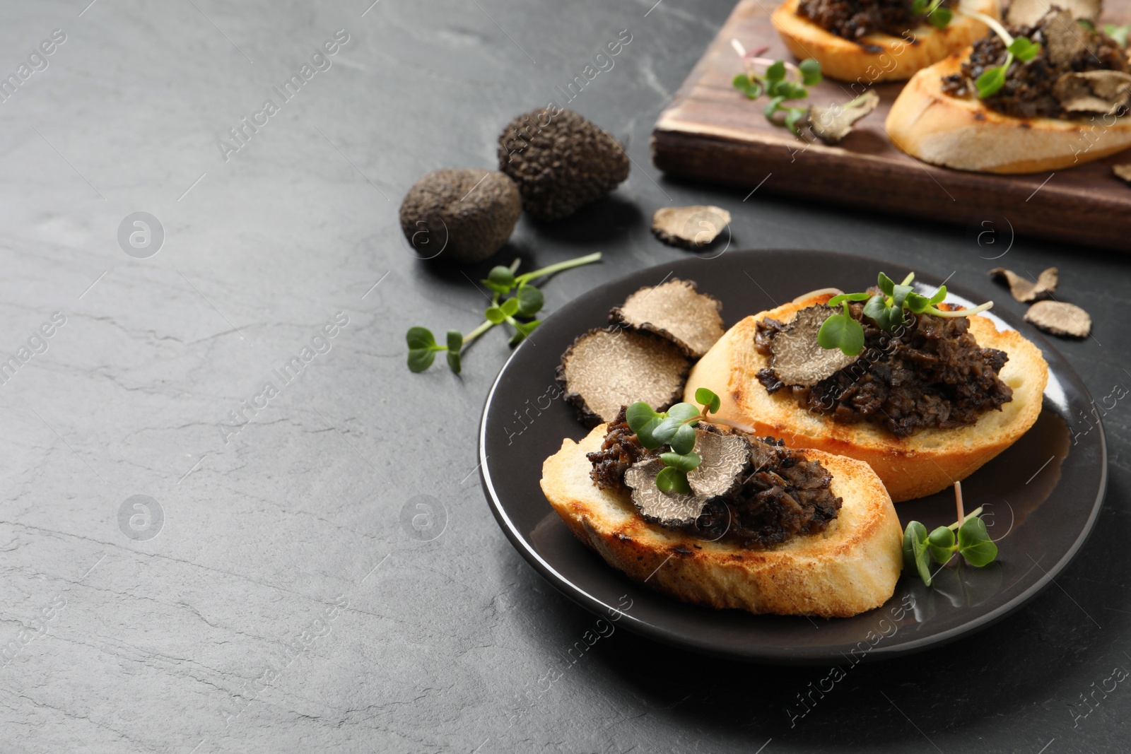 Photo of Delicious bruschettas with truffle sauce and microgreens on black table. Space for text