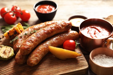 Photo of Cutting board with delicious barbecued sausages served on wooden table