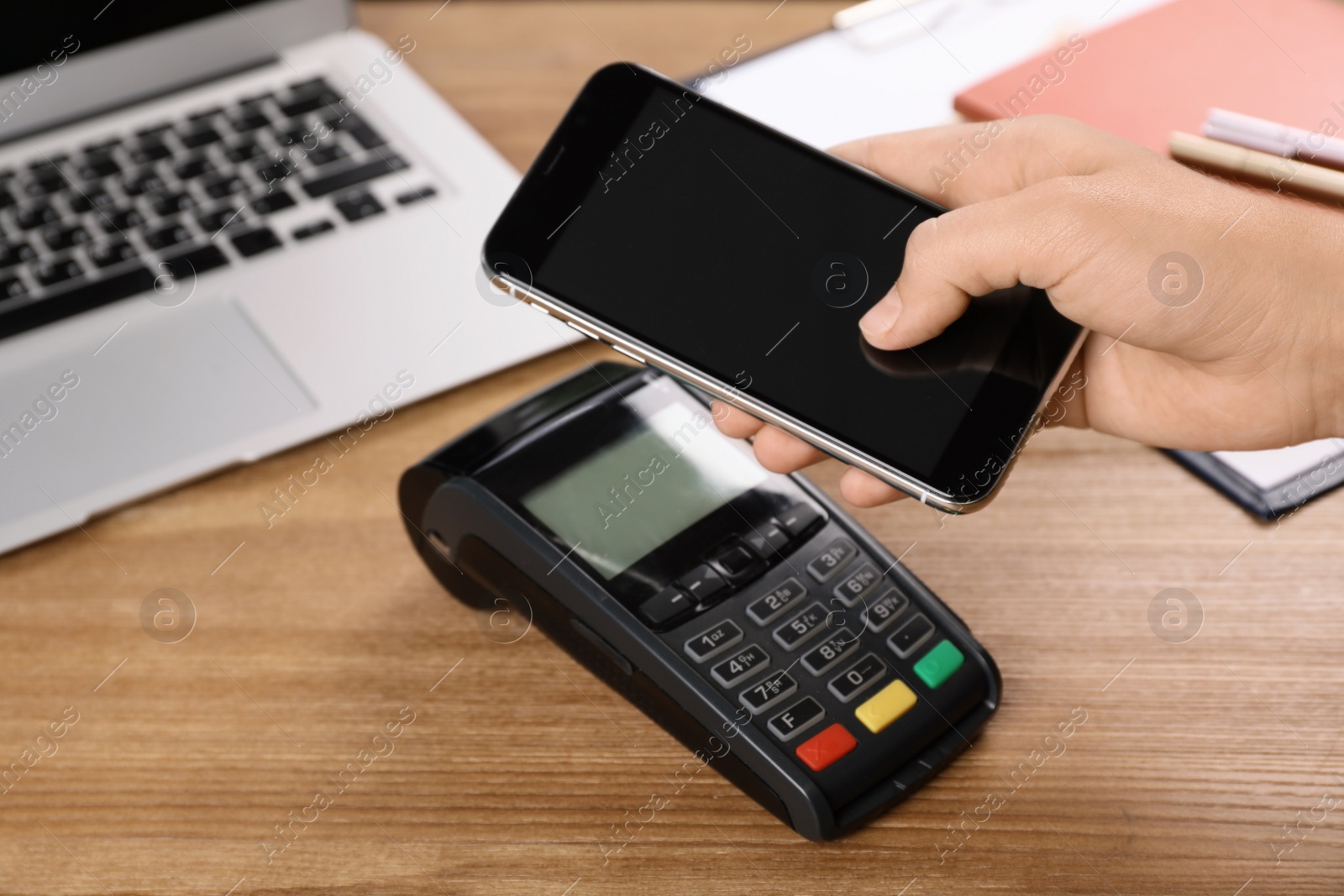 Photo of Woman using terminal for contactless payment with smartphone at table