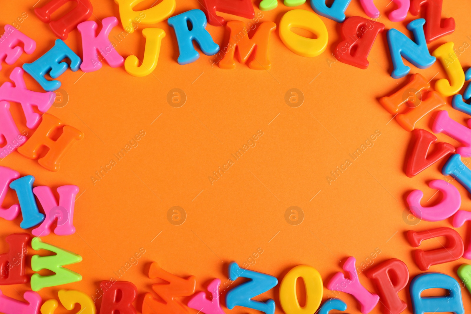 Photo of Frame made of many colorful magnetic letters on orange background, flat lay. Space for text