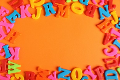 Photo of Frame made of many colorful magnetic letters on orange background, flat lay. Space for text