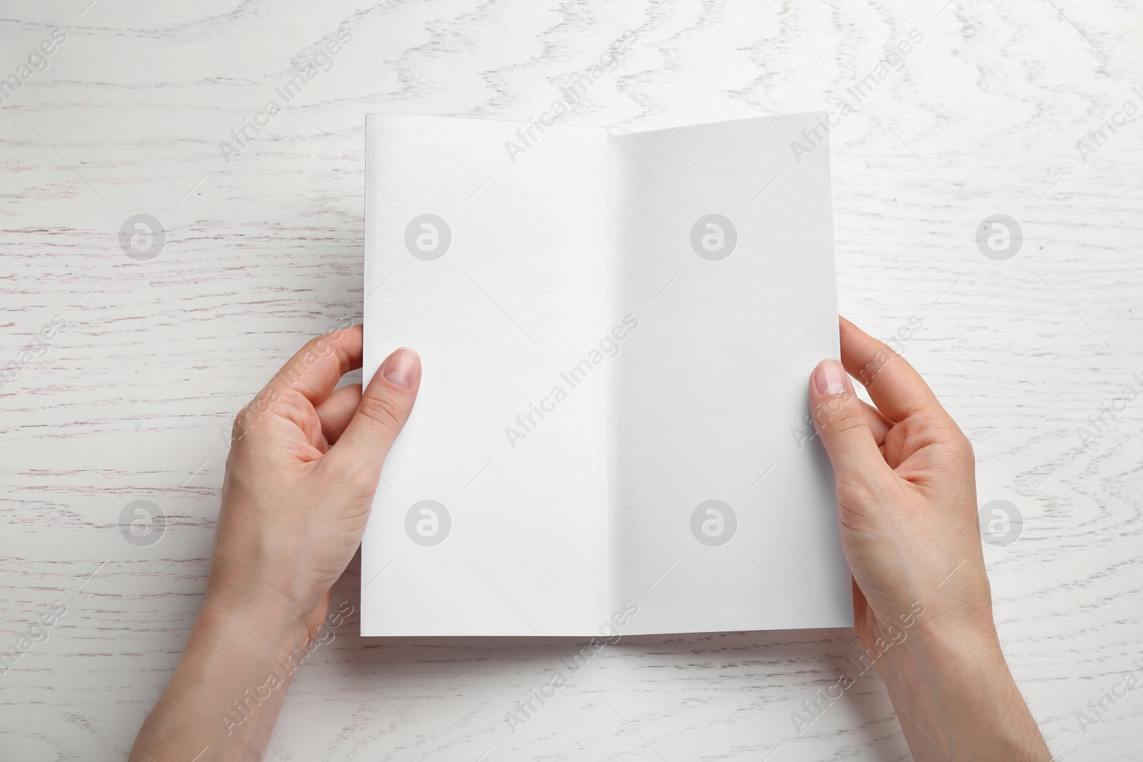 Photo of Young woman holding blank brochure at white wooden table, top view. Mock up for design