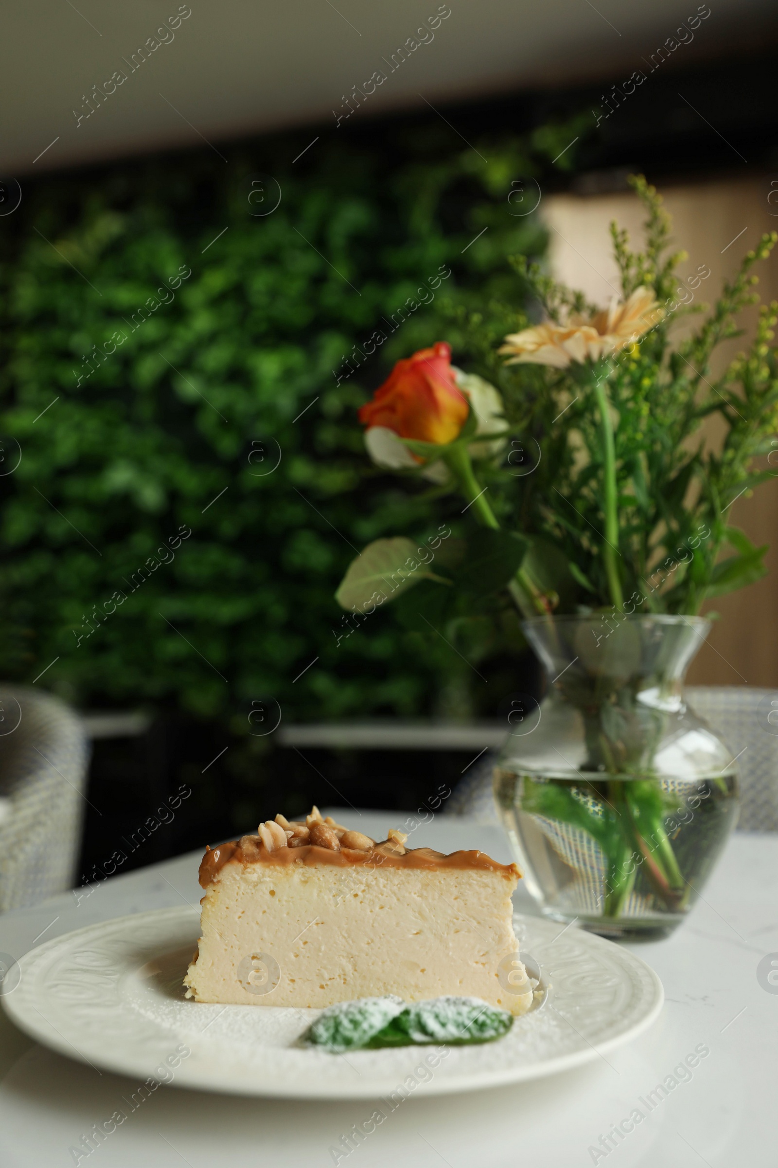 Photo of Tasty dessert and vase with flowers on white table in cafeteria