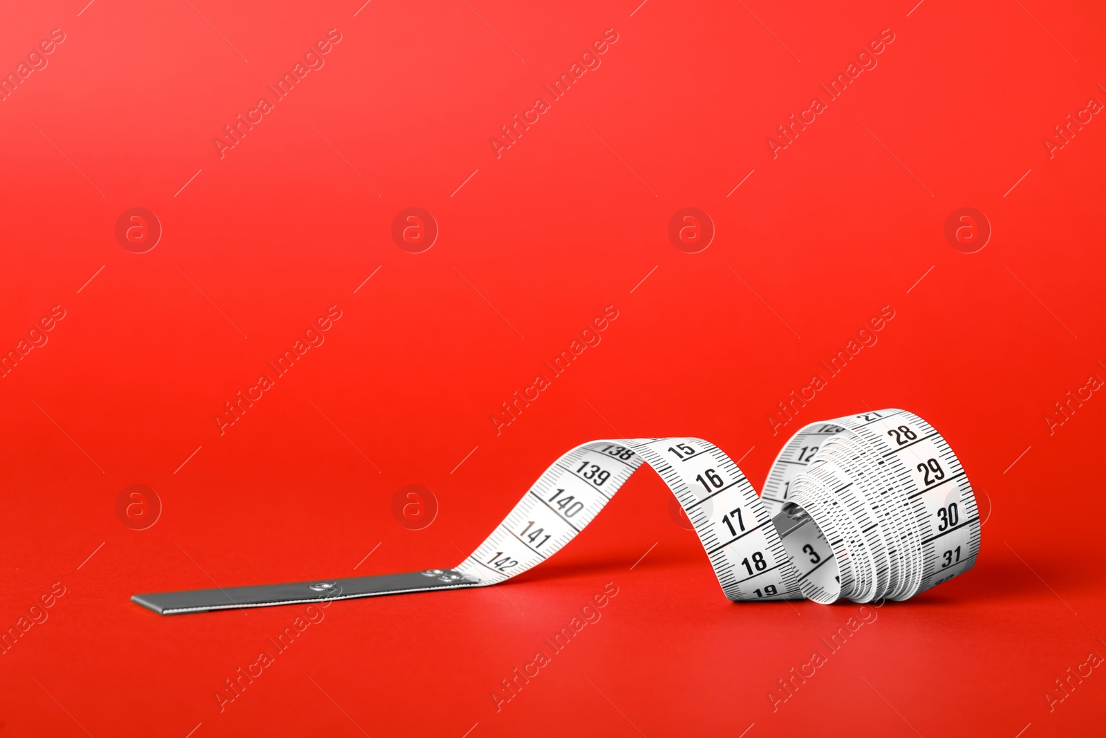 Photo of White measuring tape on red background, closeup. Space for text