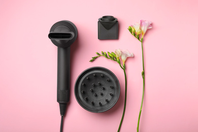 Photo of Hair dryer with different attachments on pink background, flat lay. Professional hairdresser tool