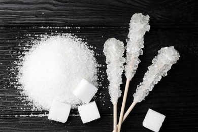 Photo of Different types of sugar on black wooden table, flat lay