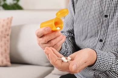 Photo of Senior man pouring pills from bottle into hand indoors, closeup
